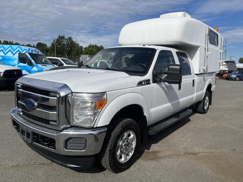 A 2014 Ford F-350 Super Duty truck with a white camper shell mounted on the bed and chrome accents on the front grille and wheels