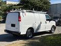 A white 2019 GMC Savana cargo van with a roof rack parked on the side of the road