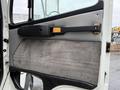 A close-up of the door panel of a 2003 Freightliner FL70 featuring a gray fabric and plastic surface with a black handle and a gold accent piece