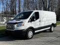 A white 2017 Ford Transit van with a black lower base and silver grille parked on a gray surface