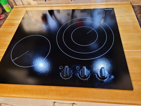 A black 3 burner cooktop featuring three control knobs and circular heating elements in a smooth surface design