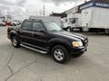 A black 2004 Ford Explorer Sport Trac with a silver step bar and alloy wheels is parked at an outdoor location