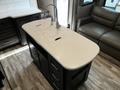 A modern kitchen island with a smooth, light-colored countertop and a sink in the center surrounded by dark cabinetry and drawers