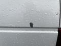 A close-up of a white 2010 Ford F-250 SD with rain droplets on its surface showing a small area of paint damage
