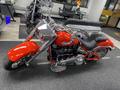 A 2024 Harley Davidson Fat Boy motorcycle in bright red with chrome accents and a low-slung seat positioned in a showroom