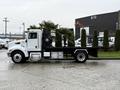 A white 2020 Peterbilt 330 flatbed truck with black accents and a storage box on the side parked on a wet surface