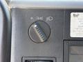 A round control knob with a vertical slider and light symbol on a textured surface near a dashboard with a visible inspection sticker and brand label