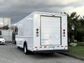 A white 2012 Ford Econoline cargo van parked at an angle with a closed roll-up door at the rear and taillights visible