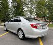 A silver 2012 Toyota Camry parked with its rear and side visible showcasing sleek lines and alloy wheels