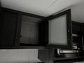 A close-up of a kitchen cabinet in a 2022 Aspen Trail camper with an open door revealing an empty compartment and a microwave below it