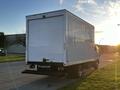 A 2017 Isuzu NPR box truck with a white rear exterior and a flatbed, positioned on a street with a sunset in the background