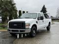 A white 2008 Ford F-250 SD pickup truck with a black grille and front bumper parked on a wet road
