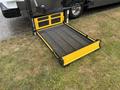 A yellow wheelchair lift with a textured mesh surface is extended in a flat position, designed for accessibility use with vehicles