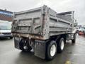 A 2003 International 5600i dump truck with a gray body and a rear dumping mechanism parked on an urban street