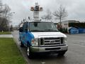 A blue 2009 Ford Econoline van with a raised platform and two orange lights on top parked on the side of a road
