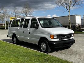 A white 2004 Ford Econoline van is parked, featuring a boxy design, four side doors, and medium-sized wheels