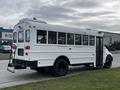 A white 2013 International 4200 school bus with multiple windows and a rear door parked on a grassy area