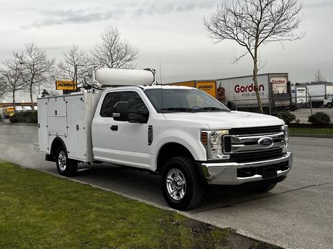 A white 2019 Ford F-350 SD with a utility body and a large storage compartment on the bed parked on a paved surface