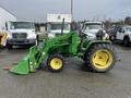 A green 2003 John Deere 790 tractor with a yellow seat and bucket attachment parked beside other trucks