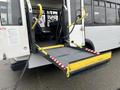 A yellow wheelchair ramp extended from the back of a 2018 Chevrolet Express bus with open doors revealing the interior seating area