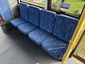 Five blue fabric bus seats with a geometric pattern arranged in a row in a public transport vehicle