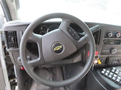Steering wheel of a 2020 Chevrolet Express with controls for audio and cruise settings visible along with dashboard instruments and gear shift console