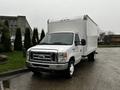 A 2017 Ford Econoline box truck with a white exterior and a large cargo area in the back parked on a wet surface