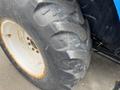 Close-up of a large, rugged tire from a 2016 New Holland T475 tractor showcasing deep treads and a white rim with some rust spots