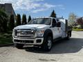 A 2016 Ford F-550 truck with a white exterior and a flatbed cargo area is parked with its headlights illuminated and chrome accents visible