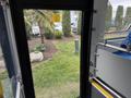 A 2018 Grande West Vicinity bus interior showing a view through the open door with blue seats and a clear view of the outside landscaping and garden area