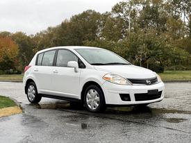 A 2012 Nissan Versa in white with a hatchback design parked on a wet surface