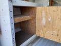 A wooden shelf and door inside a storage compartment of a 2012 GMC Savana van with a carpeted base