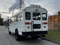 A white 2013 International 4200 school bus with rear lights and a step at the back parked on a street