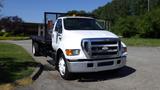 A white 2006 Ford F-650 with a flatbed design and orange lights on the roof facing forward