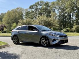 A silver 2024 Kia Forte5 is parked at an angle with stylish alloy wheels and a sporty front grille showcasing its modern design