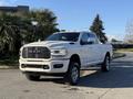 A 2023 RAM 3500 pickup truck in white with chrome accents and a bold front grille is parked on a paved surface with palm trees nearby