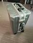A silver suitcase with a textured surface features a handle and wheels standing upright on a flat surface