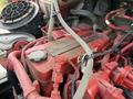 Close-up of a Cummins engine with red valve cover and various hoses and wires connected, showing detailed machinery components in a truck engine bay