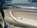 The interior door panel of a 2009 BMW X5 featuring beige leather upholstery and wood trim with a window control button