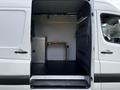 A 2017 Mercedes-Benz Sprinter van with an open side door revealing an empty interior featuring a small wooden table and minimalistic setup