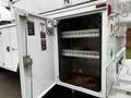 A white 2004 Ford F-450 SD service truck with an open storage compartment showing two metal shelves inside