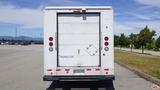 A white 2011 Ford Econoline with a closed rear door and red tail lights parked in an empty lot