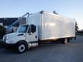 A 2014 International Durastar truck with a large white cargo box attached to its frame, parked with one wheel slightly elevated on the curb