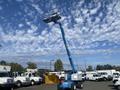 A blue 1997 Genie S-65 4X4 aerial lift with a raised platform and extended boom is positioned in the foreground