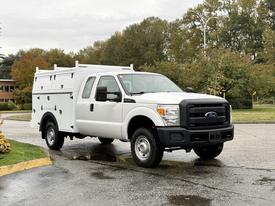 A white 2015 Ford F-350 Super Duty truck with a service body featuring multiple compartments and a black grille in the front