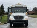 A 2016 International CE300 school bus with a white exterior and front headlights illuminated, featuring large windows and accessible doors open for entry