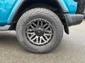 A blue 2020 Jeep Wrangler with a custom wheel and all-terrain tire in the foreground