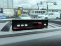 A black and red device with buttons labeled AUX FAST DIM and POWER placed on the dashboard of a vehicle