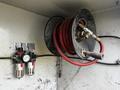 A red air hose coiled on a reel with fittings attached and connected to a pressure regulator mounted on a wall