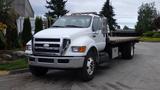 A white 2008 Ford F-750 flatbed truck with a large front grille and multiple amber lights on the roof